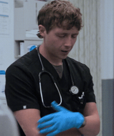 Man In Black Scrub With Stethoscope Putting On Blue Gloves GIF