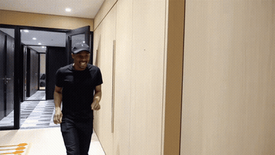Man In Black Shirt And Baseball Cap Walking Down Hallway GIF