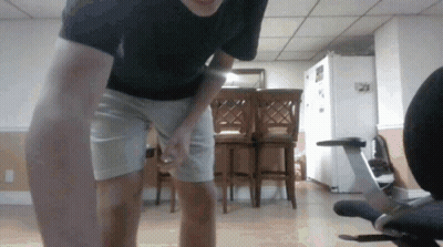 Man In Black Shirt And White Shorts Standing Before Chair GIF