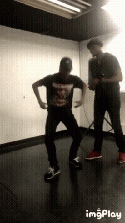 Man In Black Shirt Dancing Behind Man With Camera GIF