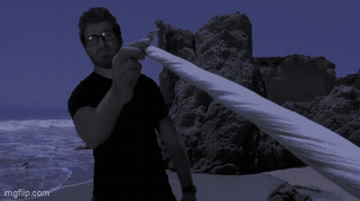 Man In Black Shirt Holding Cloth On Beach GIF
