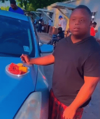 Man In Black Shirt Holding Plate Of Fruit In Front Of Car GIF
