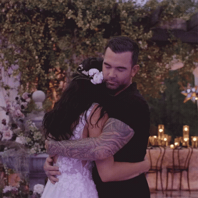 Man In Black Shirt Hugging Woman In White Dress With Flower GIF