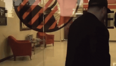 Man In Black Shirt In Front Of Glass Door With Red And Black Striped Circle GIF