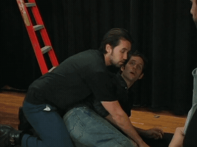 Man In Black Shirt Kneeling Next To Man In Blue Jeans GIF
