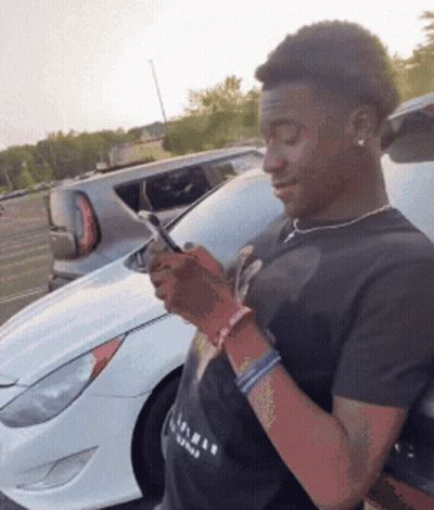Man In Black Shirt Looking At Phone Next To White Car GIF