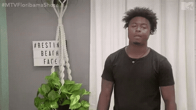 Man In Black Shirt Next To Potted Plant And Rest In Beach Face Sign GIF