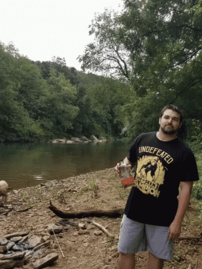 Man In Black Shirt Saying Undefeated Holds Drink GIF