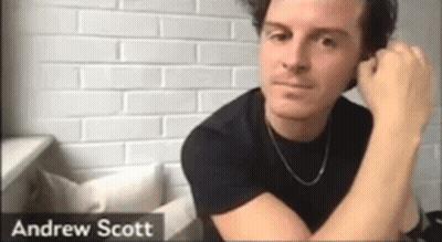 Man In Black Shirt Sitting By Brick Wall Hand On Ear GIF