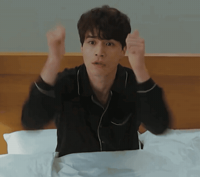 Man In Black Shirt Sitting On Bed With Arms In Air GIF