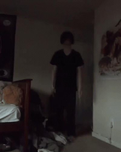 Man In Black Shirt Standing Next To Bed In Dark Room GIF