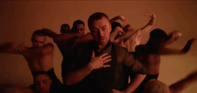 Man In Black Shirt Surrounded By Naked Men Dancing GIF