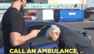 Man In Black Shirt Talking To Older Man In Blue Car Saying Call An Ambulance GIF