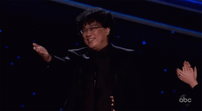 Man In Black Suit And Glasses Arms Outstretched On Stage GIF
