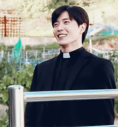 Man In Black Suit And Priest Collar Smiling Beside Fence GIF