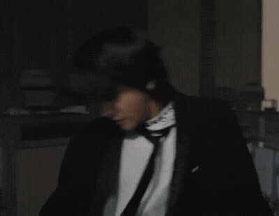 Man In Black Suit And Tie With Green Necklace GIF