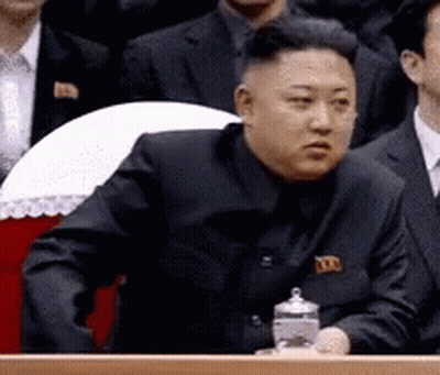 Man In Black Suit Sitting Before Group Of Men GIF