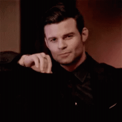 Man In Black Suit Sitting With Hand On Shoulder GIF
