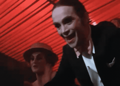 Man In Black Suit Smiling Before Red Canopy GIF