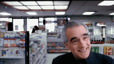 Man In Black Suit Smiling In Pharmacy GIF