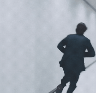 Man In Black Suit Walking Down Hallway GIF
