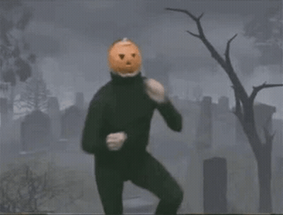 Man In Black Suit With Pumpkin Head In Cemetery GIF