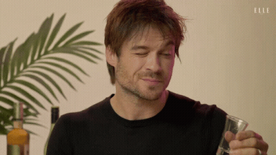 Man In Black Sweater Holds Glass, Bottle Of Elle, Palm Tree GIF
