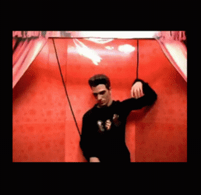 Man In Black Sweater In Front Of Red Wall GIF