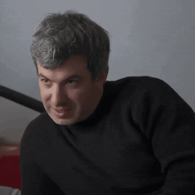 Man In Black Sweater Looks At Camera GIF