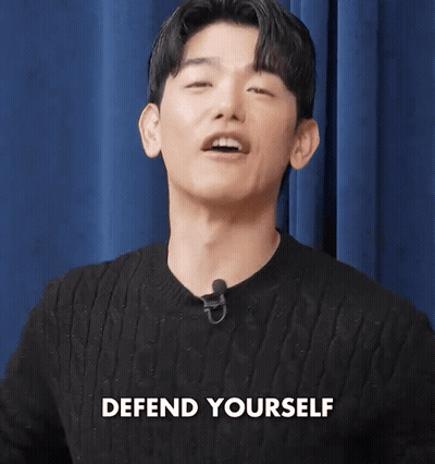 Man In Black Sweater With Microphone Says Defend Yourself GIF
