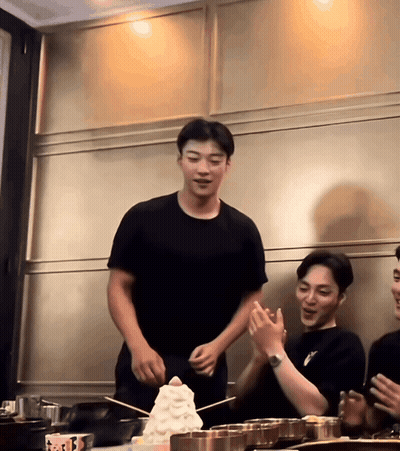 Man In Black T-Shirt Standing In Front Of Ice Cream Stack GIF