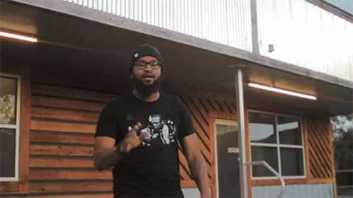Man In Black T-Shirt With Skull Standing In Front Of Building GIF