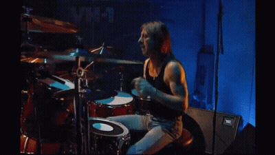 Man in Black Tank Top Playing Drums in Front of VH-1 Sign
