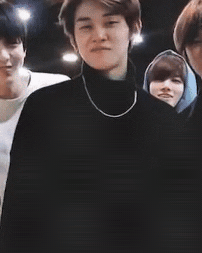 Man In Black Turtleneck And Necklace Standing Before Group GIF