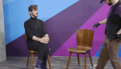 Man In Black Turtleneck Sitting While Another Man Walks By GIF