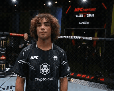 Man In Black UFC Shirt In Front Of Poleon Screen GIF