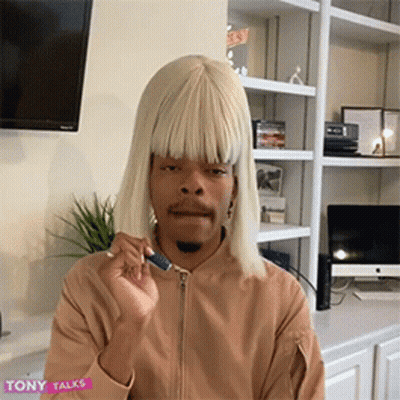 Man In Blonde Wig And Tan Jacket Sitting GIF