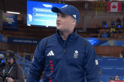 Man In Blue Adidas Jacket In Front Of Milano Cortina Screen GIF