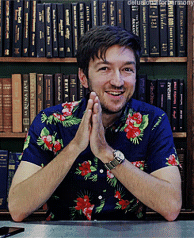 Man In Blue Floral Shirt Smiling At Bookshelf GIF
