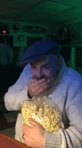Man In Blue Hat Holding Popcorn Covering Mouth GIF