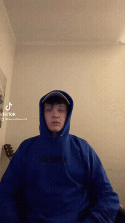 Man In Blue Hoodie And Hat Sitting By Guitar GIF