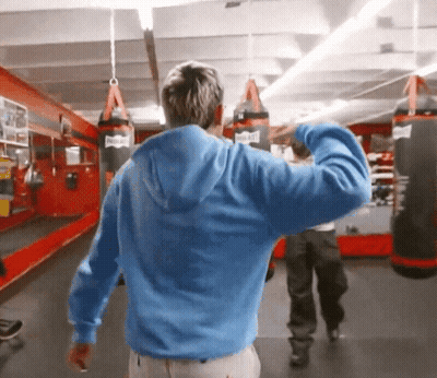 Man In Blue Hoodie In Gym With Everlast Punching Bags GIF