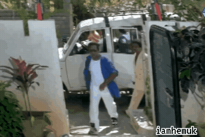 Man In Blue Jacket And White Pants Walking Past Van With Iamhamuk Sign GIF