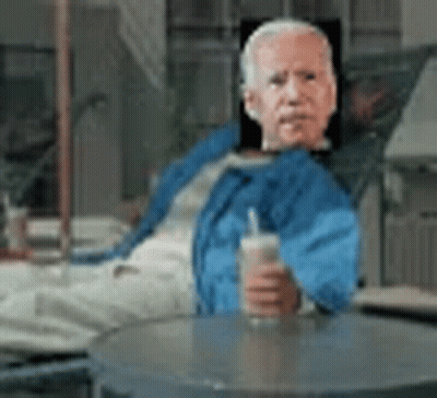Man In Blue Jacket Sitting At Table With Drink GIF