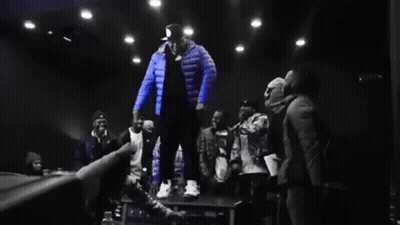 Man In Blue Jacket Standing On Table In Front Of Crowd GIF