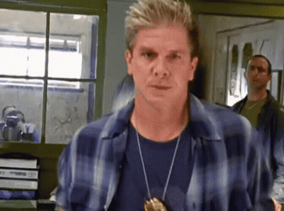 Man In Blue Plaid Shirt And Badge By Window GIF