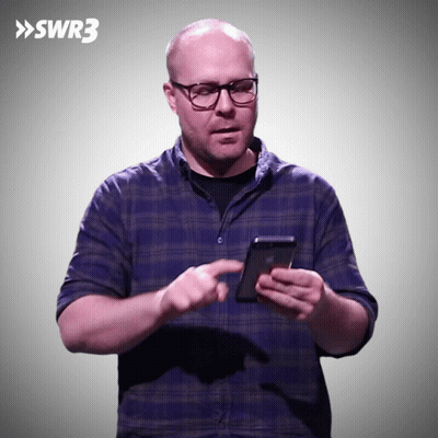 Man In Blue Plaid Shirt Holding Phone In Front Of SWR3 Sign GIF