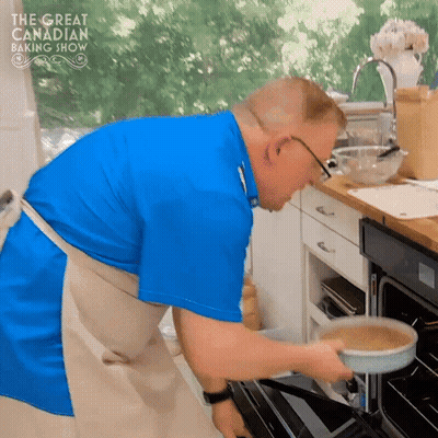 Man In Blue Shirt And Apron Putting Pan In Oven Great Canadian Baking Show GIF