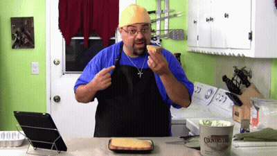 Man In Blue Shirt And Black Apron Holding Cornbread GIF