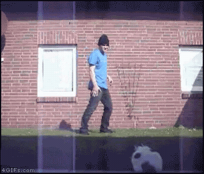 Man In Blue Shirt And Black Hat Walking By Brick Building GIF